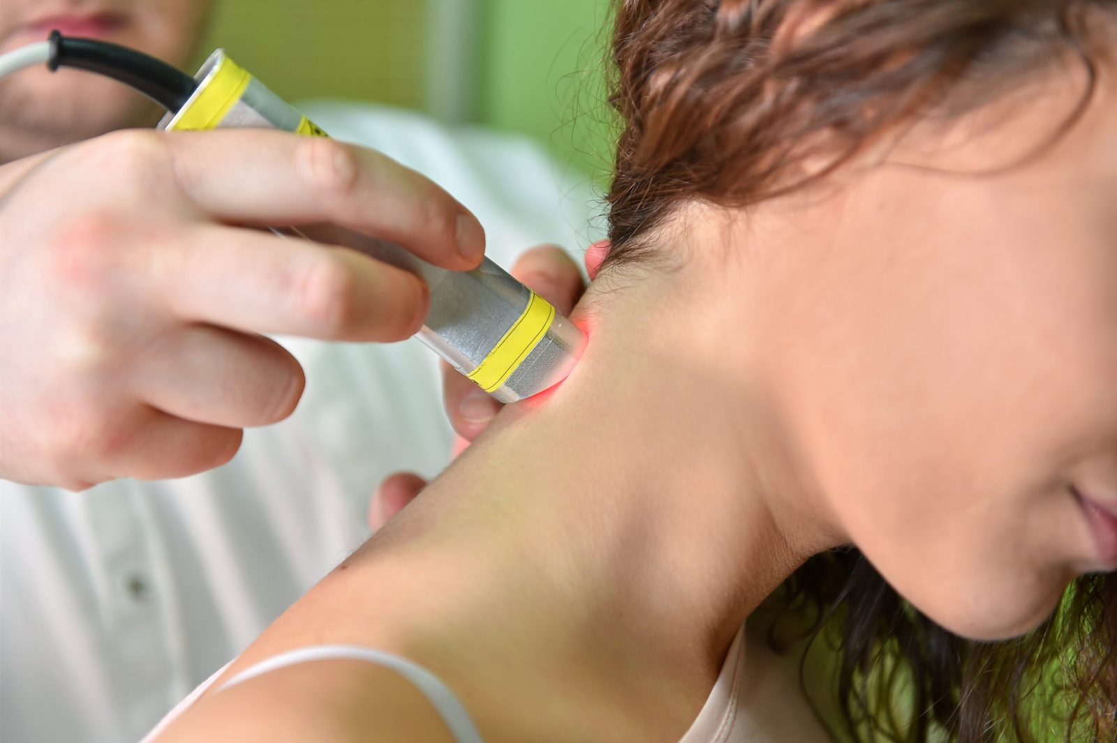 Clinician holding a handheld laser therapy probe with a red treatment beam against the back of a patient's neck — the subject of Physical Therapy 201: Laser Therapy, a two-hour chiropractic CE course from CCEDseminars
