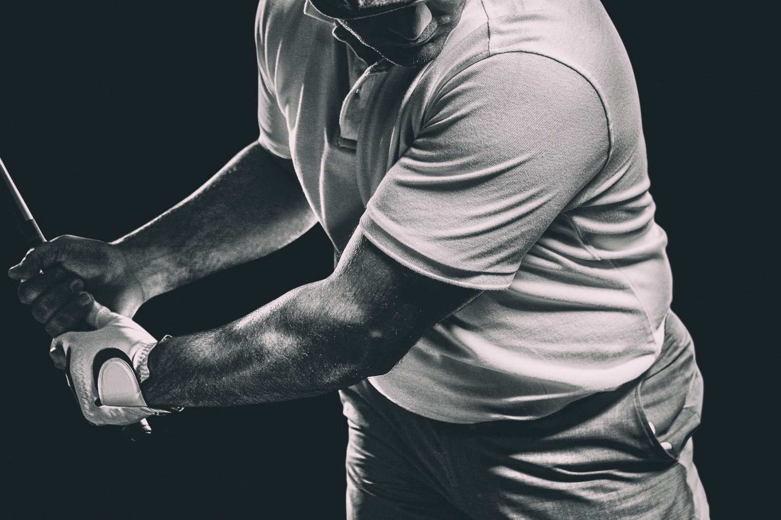 Dramatic monochrome close-up of a golfer's gloved grip, forearms, and lead shoulder mid-swing &mdash; Athletic Injuries 211: Upper Body Golf Injuries online chiropractic sports medicine CE course