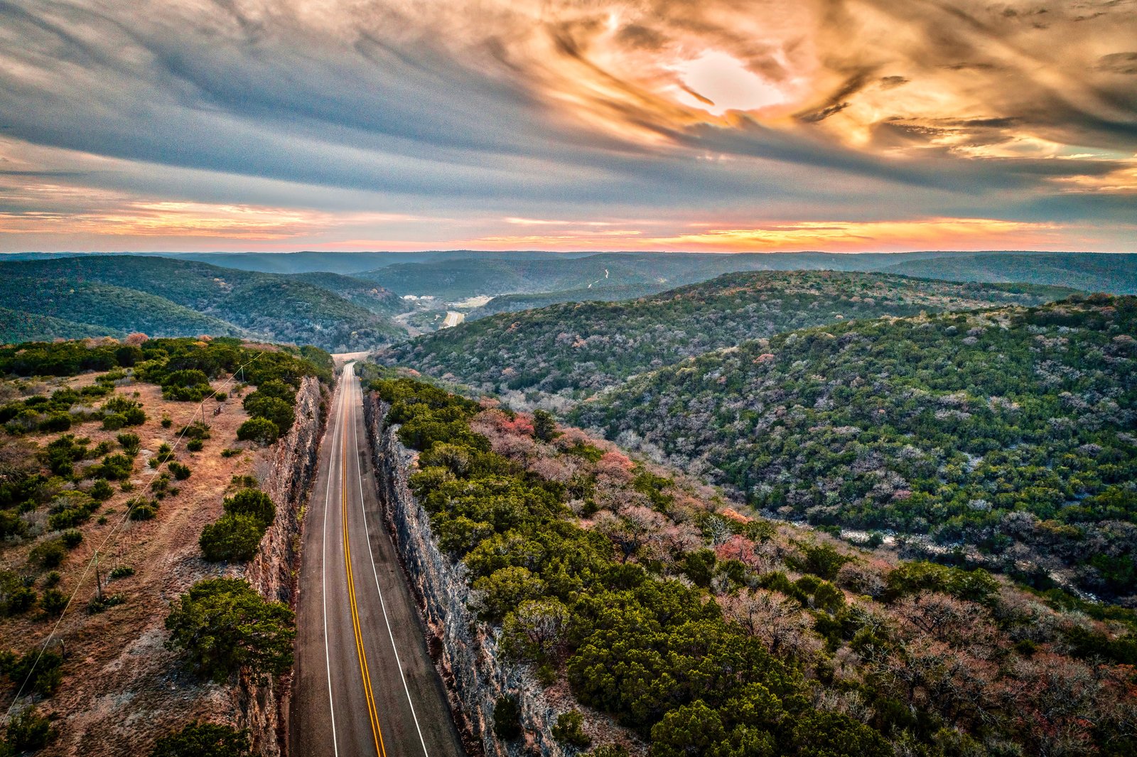 Aerial view of a two-lane road cutting through Texas Hill Country limestone cliffs at sunset — Texas TBCE chiropractic continuing education guidelines page by CCEDseminars