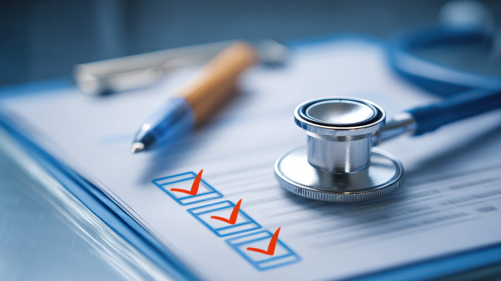 Close-up of a clinical checklist on a clipboard with three red checkmarks ticked in blue boxes, a pen and a stethoscope resting alongside