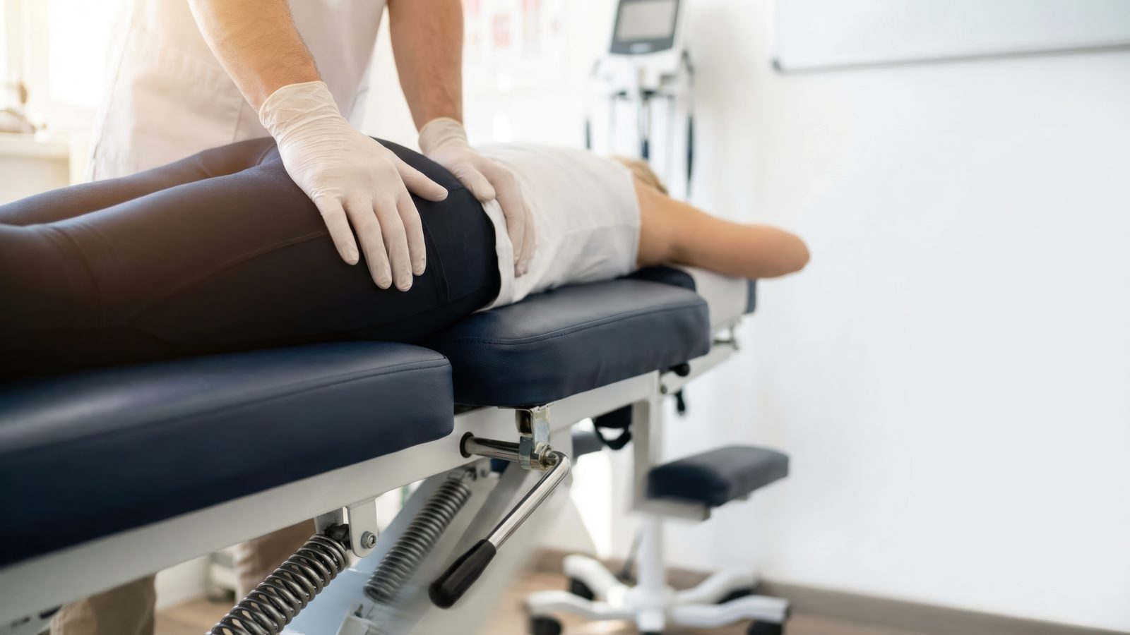 Chiropractor with hands on the pelvis of a prone patient on a segmented drop table with drop-piece springs visible — Adjusting & Manual Therapy 210: Drop Table Technique online chiropractic CE course