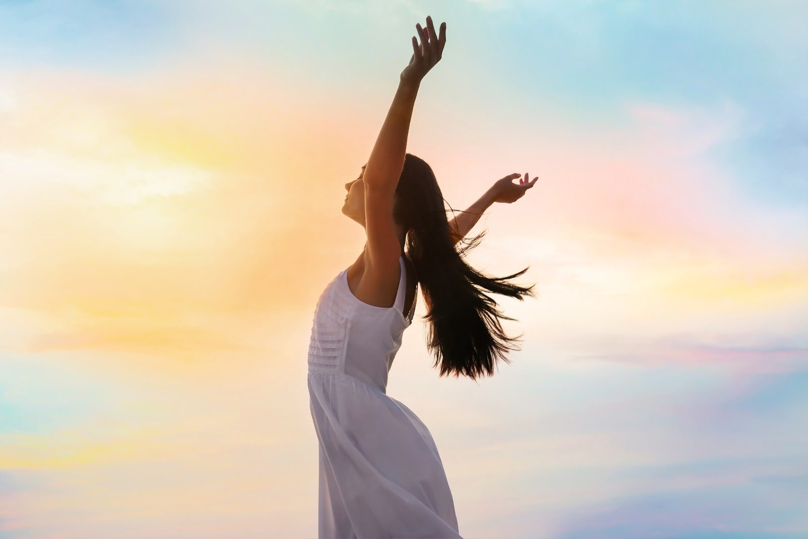 A woman in white standing with her arms raised against a warm sunset sky — the strength, bone and cardiovascular health through the menopause transition that Nutrition 226 teaches chiropractors to support as estrogen declines