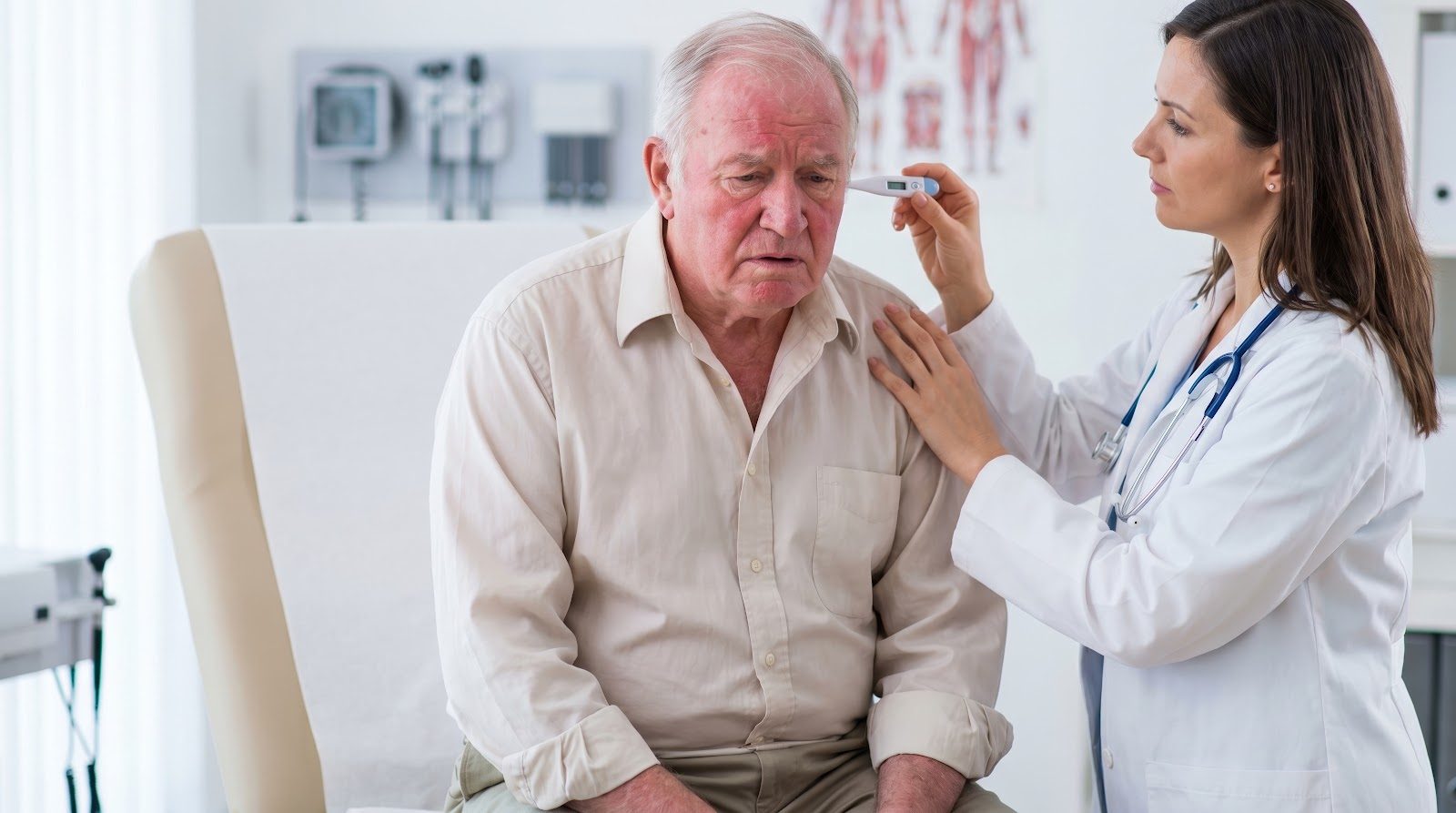 An older, flushed man seated on an exam table while a physician checks his temperature with an ear thermometer — the fatigued patient whose thyroid, adrenal and mitochondrial drivers Nutrition 228 teaches chiropractors to assess and treat nutritionally