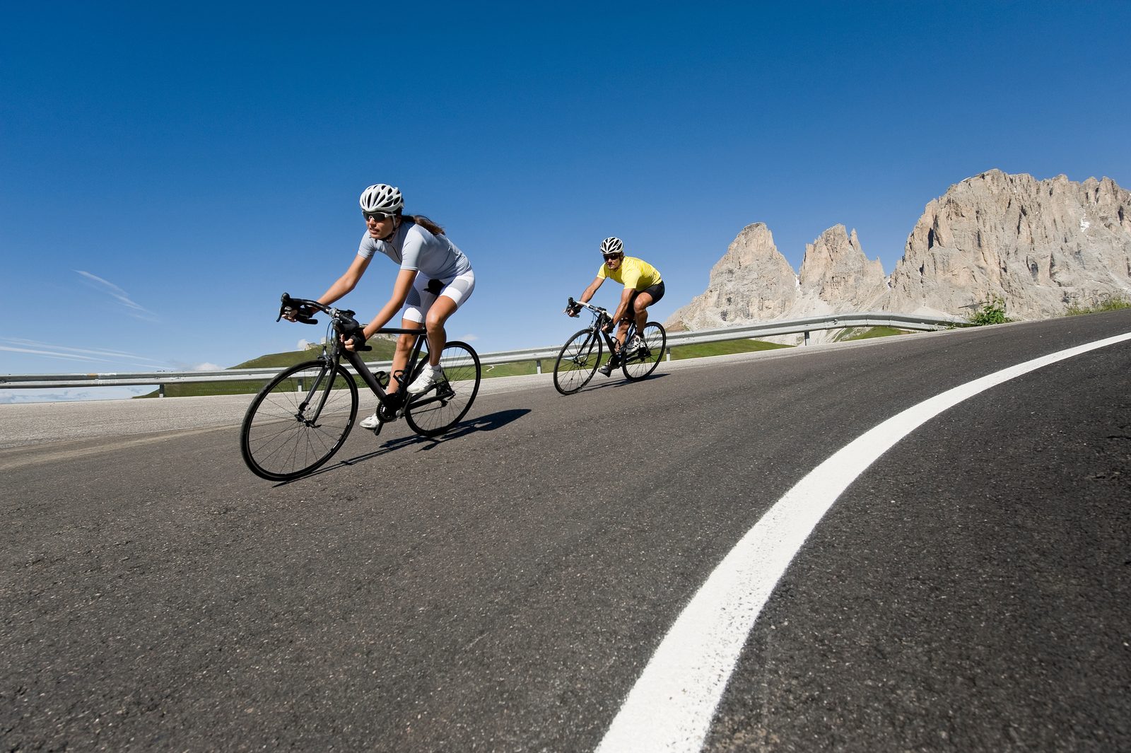 Two road cyclists in helmets descending a curving mountain highway beneath jagged peaks &mdash; Athletic Injuries 210: The Triathlete online chiropractic sports medicine CE course