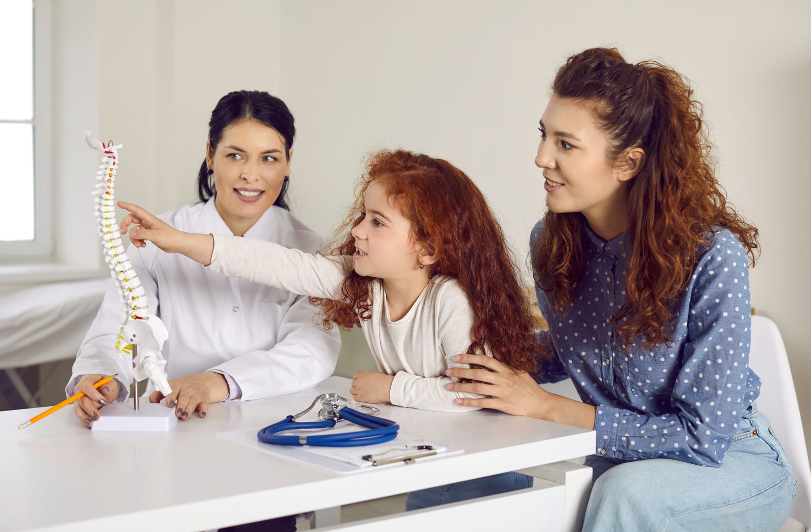 Young girl pointing at a spine model as a smiling clinician holds it and her mother looks on — Pediatrics 203: Adjusting & Office Procedures I, a 2-hour chiropractic CE course