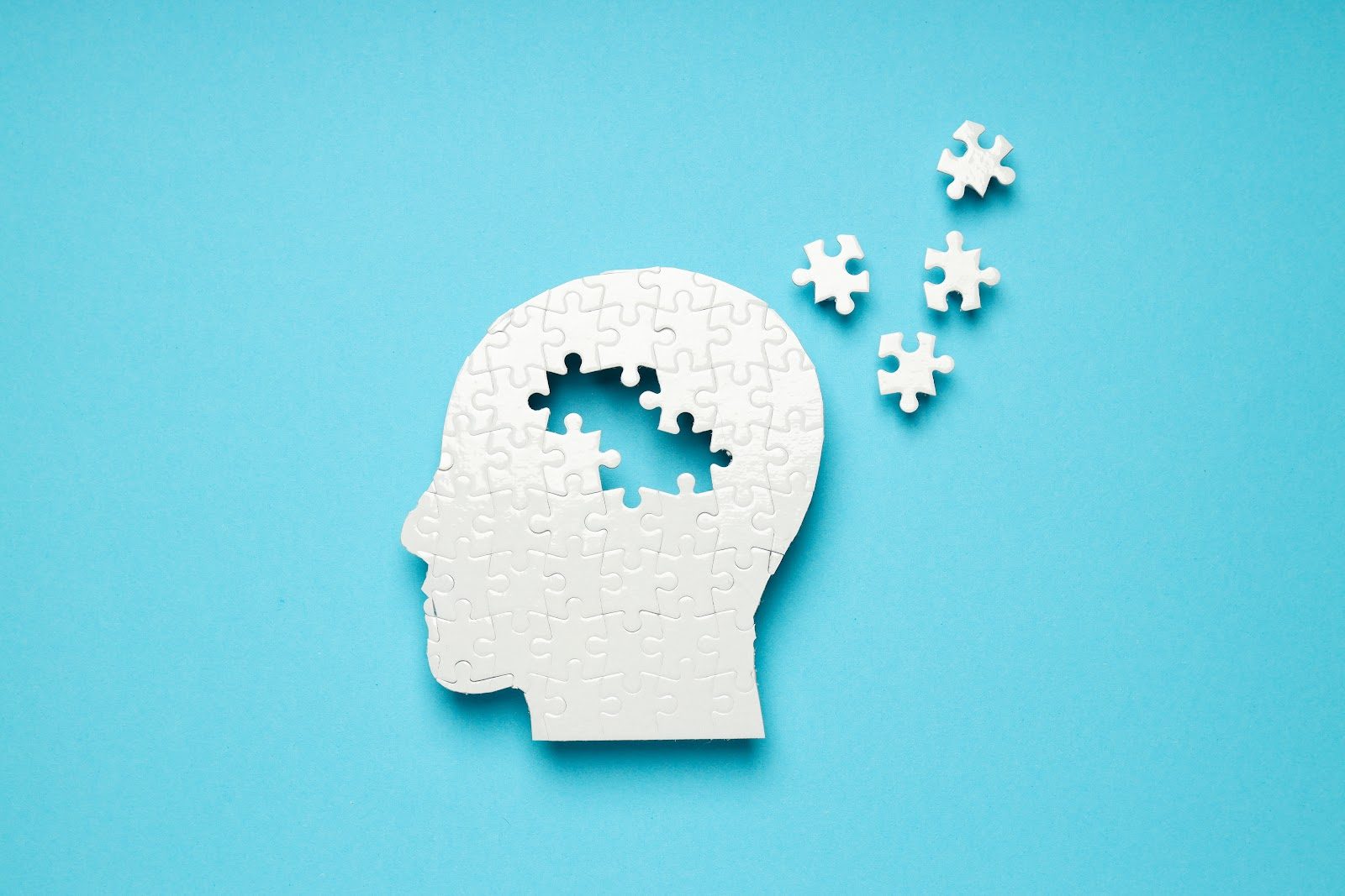 A white jigsaw-puzzle silhouette of a human head on a blue background with several pieces missing from the brain area — the memory loss and cognitive decline that Nutrition 233 teaches chiropractors to address through brain homeostasis, diet, exercise and supplementation