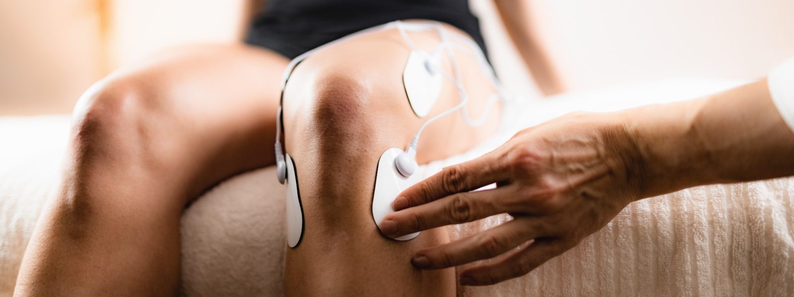 Chiropractic assistant positioning TENS electrodes on a patient’s knee during therapy.