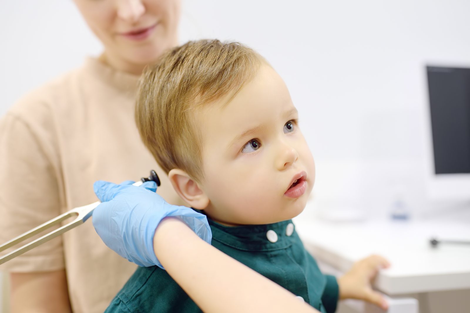 Gloved clinician using a tuning fork during a toddler's neurological exam while a parent looks on — Pediatrics 202: 3 Key Neurological Pearls for Family Practice, a 2-hour chiropractic CE course