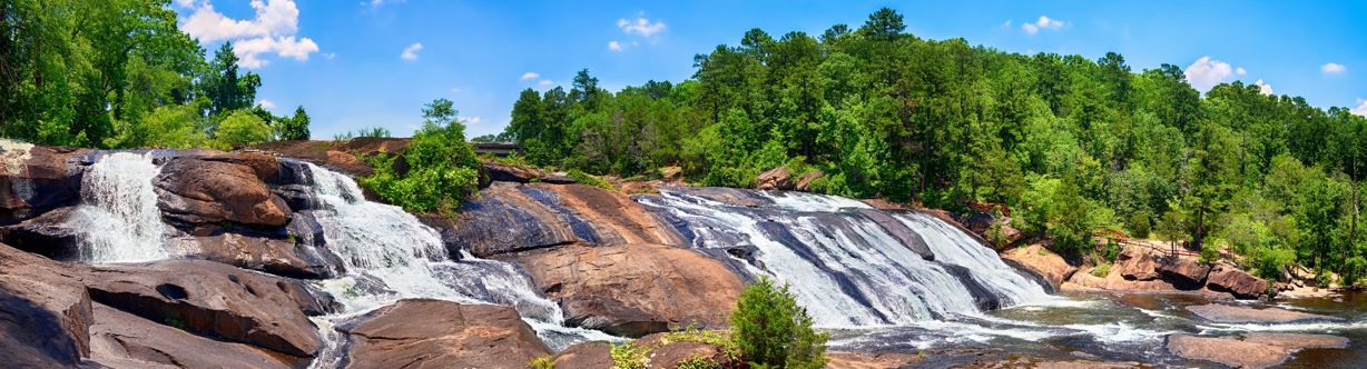 Scenic view of cascading waterfalls at High Falls State Park, Georgia, surrounded by lush green forest and blue skies