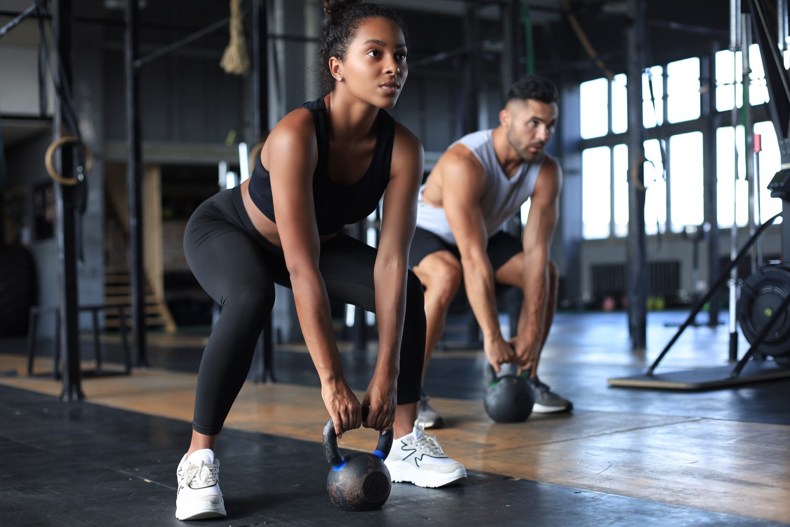 Two athletes in a gym at the bottom of a kettlebell swing setup, hips hinged with kettlebells on the floor &mdash; Athletic Injuries 209: Exercise Injuries online chiropractic sports medicine CE course