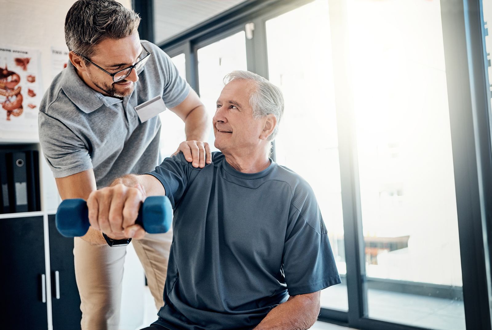 Clinician guiding an older man through a seated dumbbell shoulder raise in a bright rehab clinic, one hand steadying the shoulder, anatomy charts on the wall — Case Studies & Clinical Pearls 203: Upper Extremities online chiropractic CE course