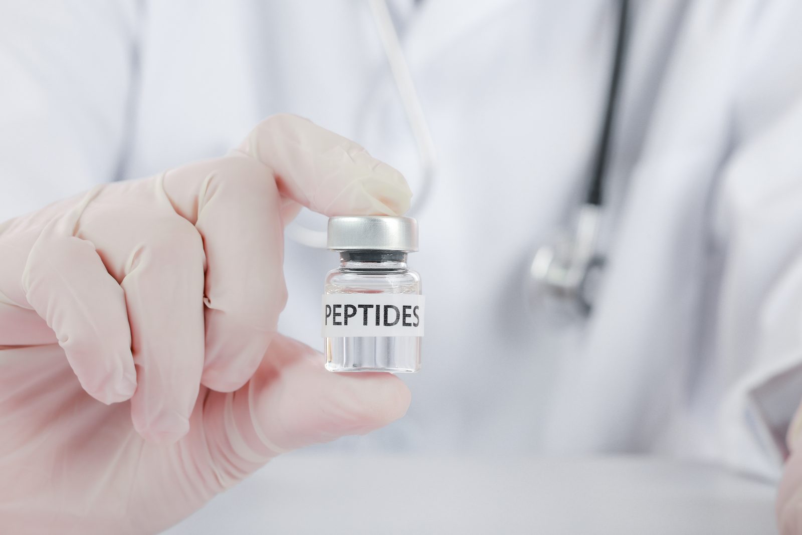 Gloved hand of a clinician in a white coat holding a small glass vial labeled PEPTIDES — Peptides & Chiropractic Practice: Evidence, Applications & Clinical Considerations, live chiropractic CE webinar with Dr. Howard Benedikt, CCEDseminars