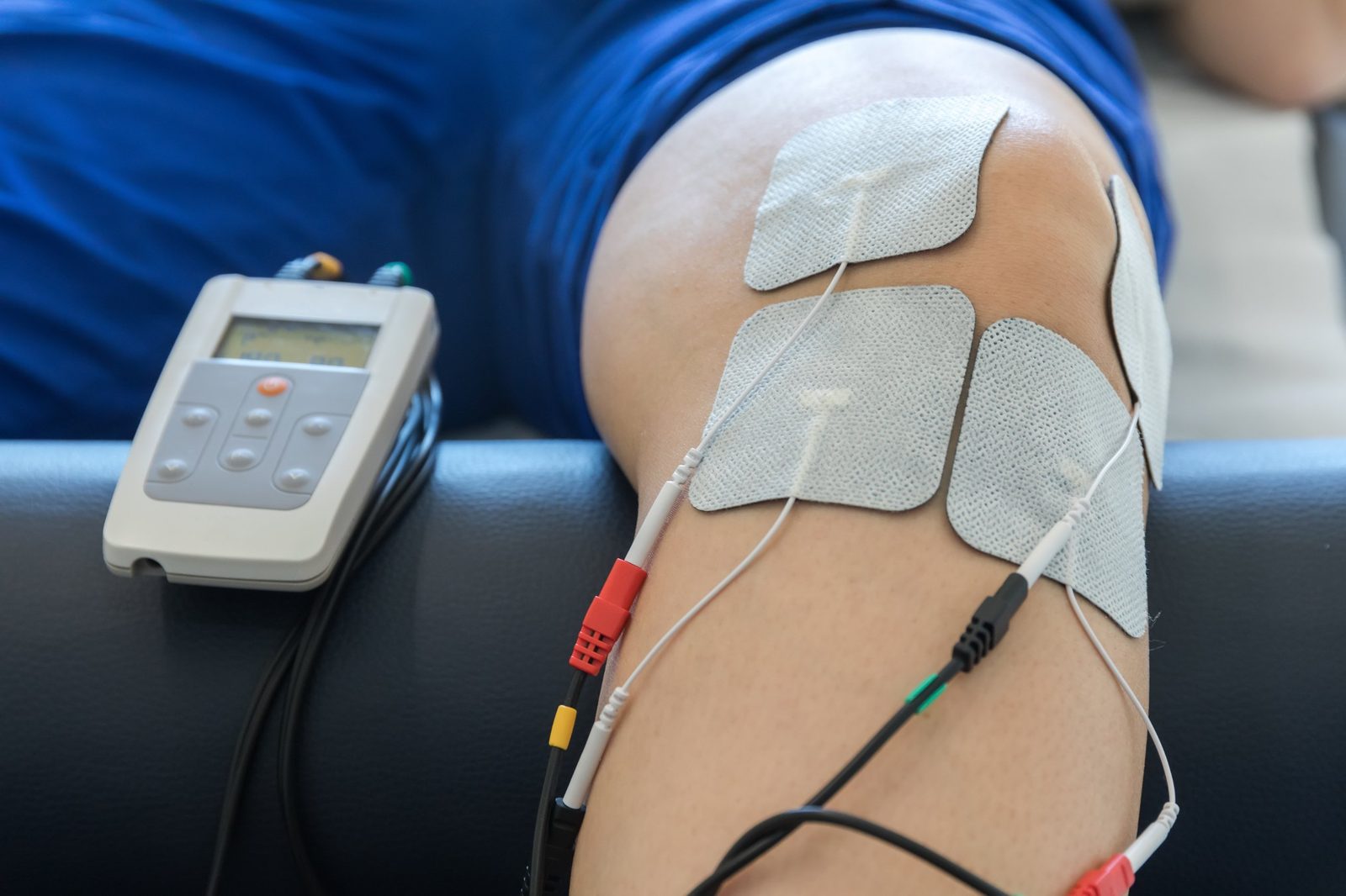 Four TENS electrode pads placed around a patient's knee, wired to a handheld TENS unit on the treatment table — the subject of Physical Therapy 202: TENS for Pain Management, a free one-hour chiropractic CE course from CCEDseminars
