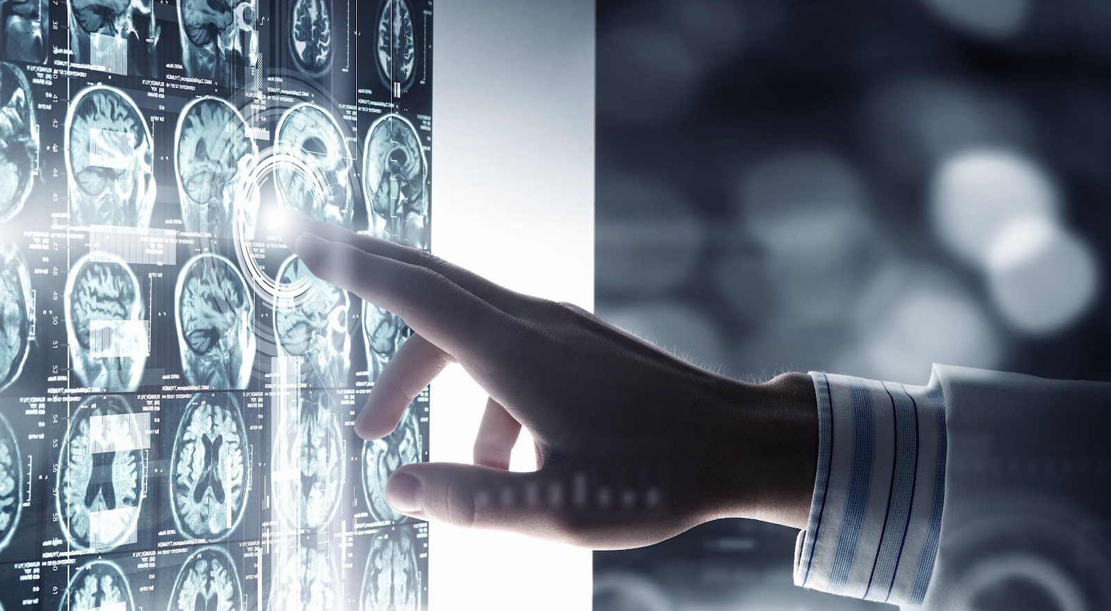 Clinician’s hand reaching toward a backlit array of brain MRI cross-sections on an illuminated display, a point of light where the fingertip meets the image — Evidence-Based Practice 204: Imaging in Clinical Practice II.