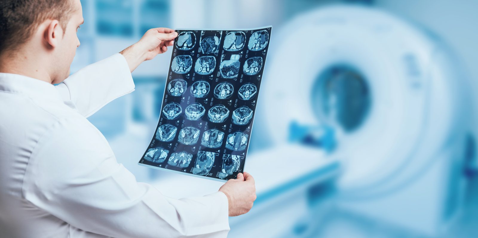 Radiologist in a white coat holding a sheet of CT cross-sectional images up to the light in front of a scanner gantry — Evidence-Based Practice 203: Imaging in Clinical Practice I.