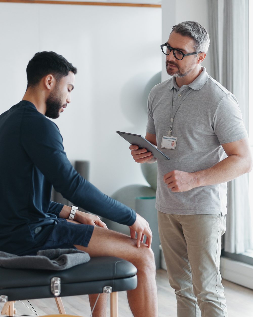 Clinician with tablet consulting a patient on a rehab table about a knee condition — chiropractic rehabilitation CE courses; CCEDseminars category page