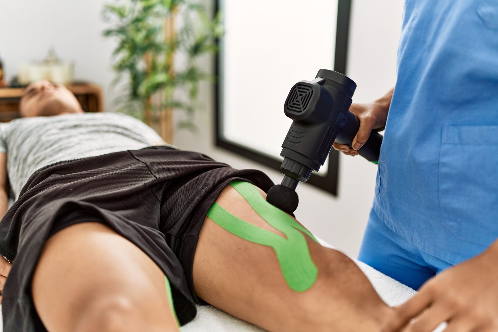 Clinician applying percussion massage therapy to a patient's kinesio-taped thigh and knee — Adjusting & Manual Therapy 206: Hip, Thigh & Knee online chiropractic CE course