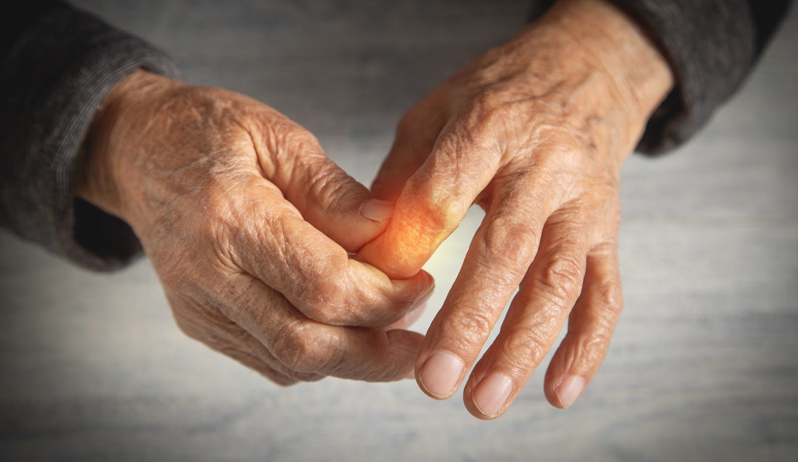 Close-up of an older person&rsquo;s hands, one hand supporting the other with the thumb and index finger joints glowing red to indicate pain