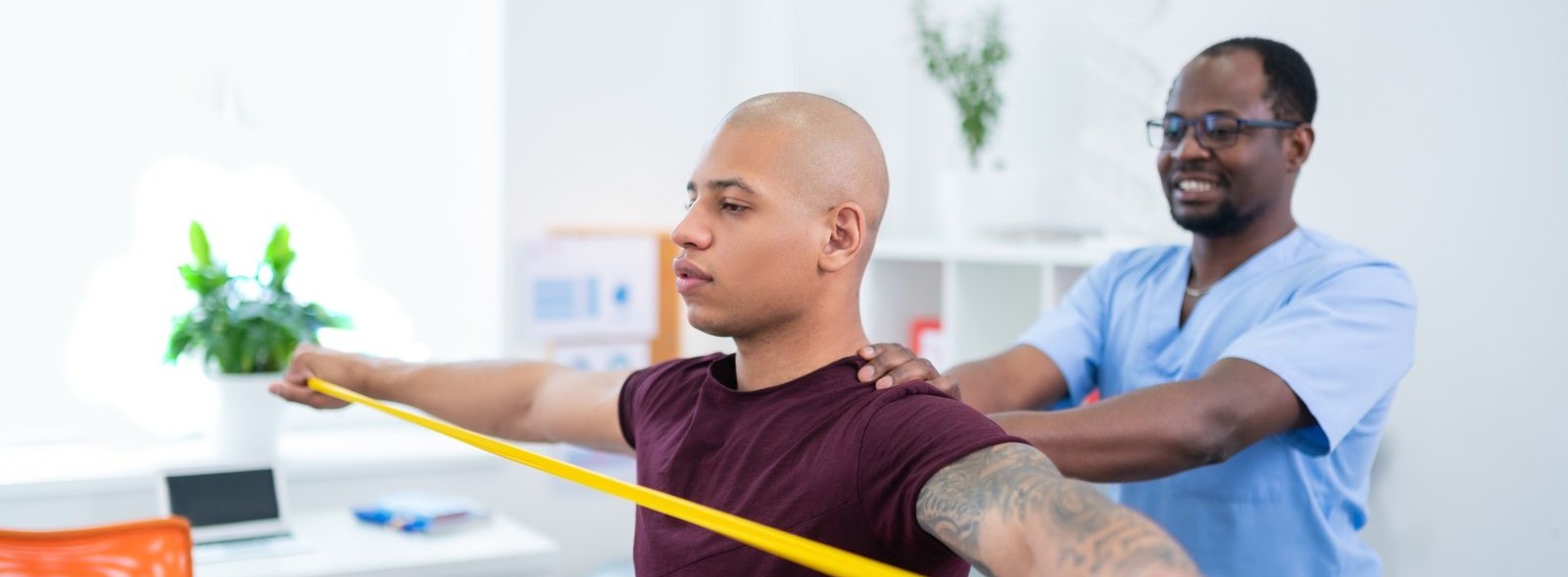 Certified chiropractic assistant guiding patient through resistance band shoulder exercise in a modern clinic