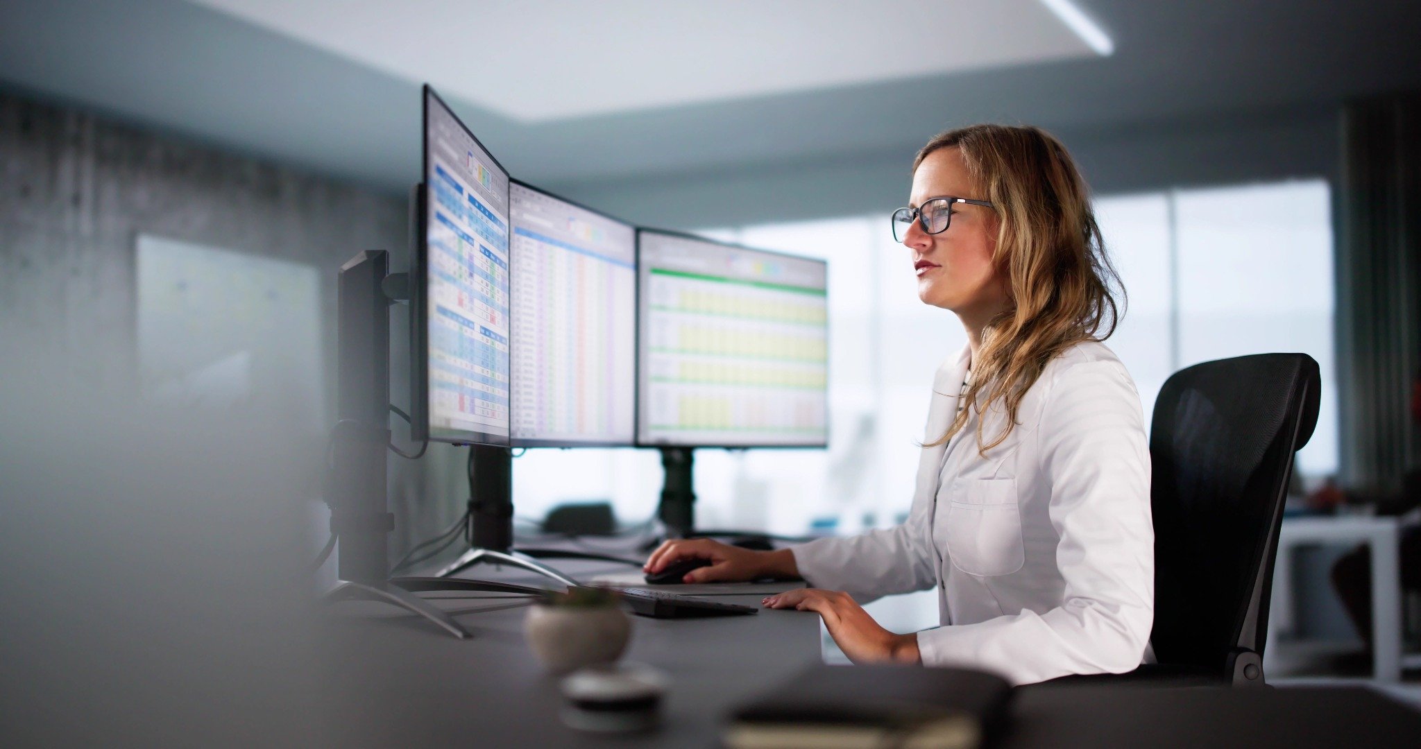 Female professional analyzing chiropractic CE analytics on dual monitors in modern office