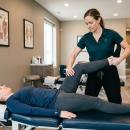 Chiropractor performing partner assisted leg stretch on patient lying supine on treatment table in a modern chiropractic office