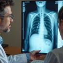 Two clinicians in white coats reviewing a chest radiograph on a monitor, the doctor pointing a pen at the lower ribs and thoracic spine — the thoracic spine and rib cage examination, the subject of Physical Examination 207: Thoracic Spine and Rib Cage, a two-hour chiropractic CE course from CCEDseminars