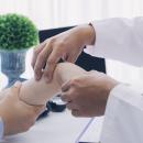 A clinician's hands palpate a seated patient's wrist while stabilizing the closed hand in a bright consultation room — the hands-on orthopedic testing taught in Physical Examination 214: Wrist, Hand and Thumb, a two-hour chiropractic CE course from CCEDseminars